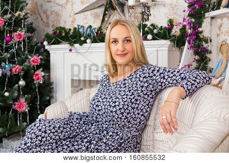 Beautiful lady sitting on sofa in room decorated for Christmas holidays