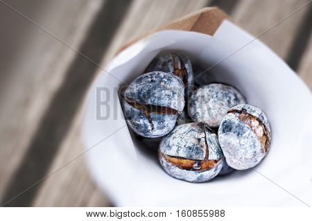 Roasted chestnuts on rustic wooden table in white paper bag with copy space