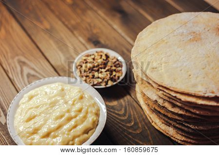 ingredients for baking homemade cake. shortcakes, buttercream or cream and nuts on a plate on vintage wooden kitchen table. copyspace for cook recipe.