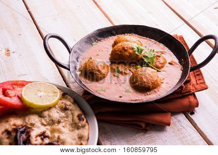 Freshly cooked spicy potato curry in frying pan or Hot and spicy Dum aloo served with tandoori roti or naan or indian bread or chapati and green salad, selective focus
