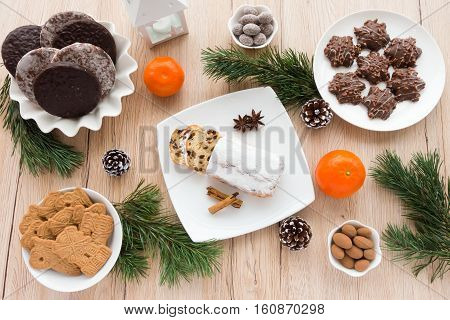 Arrangement of Gingerbread Spiced Biscuits and Mini Christstollen on light wooden background surrounded by Christmas decoration.
