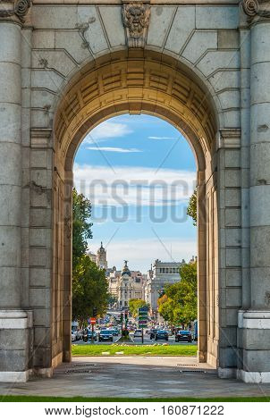 View of Metropolis building in Madrid, through an arch of the Plaza de la Independencia Monument.   Urban life, traffic flows in a busy, mid-day street scene.