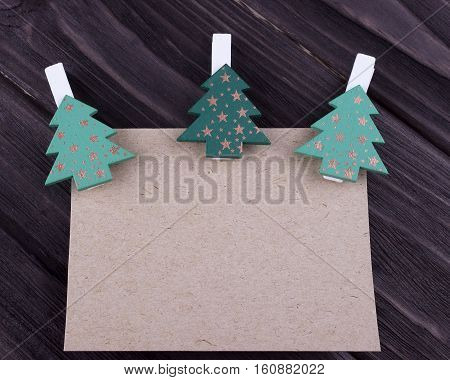 Christmas Xmas New Year Holiday greeting card concept with emty sheet of cardboard three Christmas tree on clothespins on dark wooden background space for text