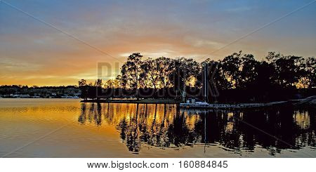 Tranquil Dawn - Orange and gold sunrise over water with skyline tree silhouettes has clear water reflections Photographed at Rathmines Lake Macquarie New South Wales Australia.