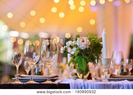 Wedding. Banquet. The chairs and table for guests decorated with candles served with cutlery and crockery and covered with a tablecloth.