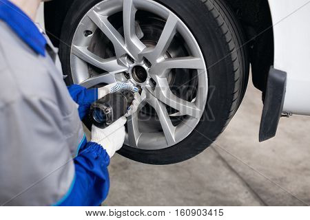 car mechanic screwing or unscrewing car wheel of lifted automobile by pneumatic wrench at repair service station