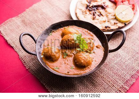 Freshly cooked spicy potato curry in frying pan or Hot and spicy Dum aloo served with tandoori roti or naan or indian bread or chapati and green salad, selective focus