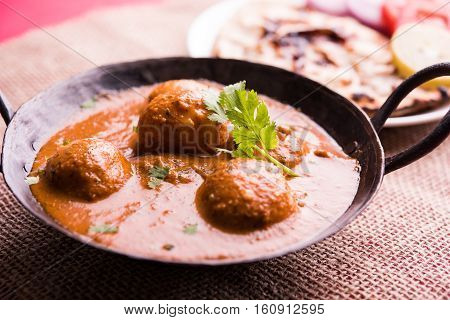 Freshly cooked spicy potato curry in frying pan or Hot and spicy Dum aloo served with tandoori roti or naan or indian bread or chapati and green salad, selective focus