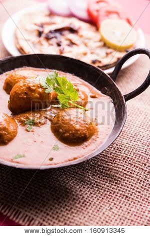 Freshly cooked spicy potato curry in frying pan or Hot and spicy Dum aloo served with tandoori roti or naan or indian bread or chapati and green salad, selective focus