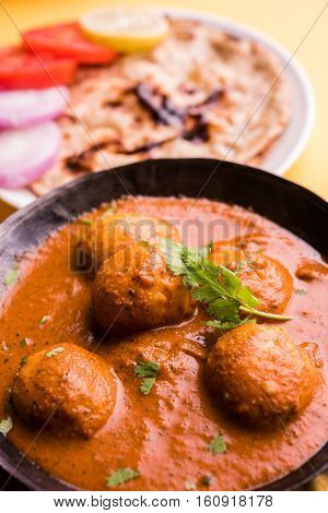 Freshly cooked spicy potato curry in frying pan or Hot and spicy Dum aloo served with tandoori roti or naan or indian bread or chapati and green salad, selective focus