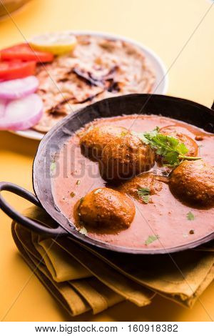 Freshly cooked spicy potato curry in frying pan or Hot and spicy Dum aloo served with tandoori roti or naan or indian bread or chapati and green salad, selective focus