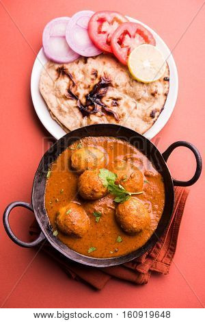 Freshly cooked spicy potato curry in frying pan or Hot and spicy Dum aloo served with tandoori roti or naan or indian bread or chapati and green salad, selective focus
