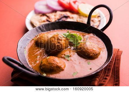 Freshly cooked spicy potato curry in frying pan or Hot and spicy Dum aloo served with tandoori roti or naan or indian bread or chapati and green salad, selective focus
