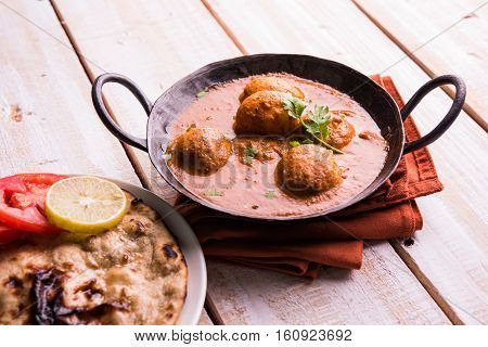 Freshly cooked spicy potato curry in frying pan or Hot and spicy Dum aloo served with tandoori roti or naan or indian bread or chapati and green salad, selective focus