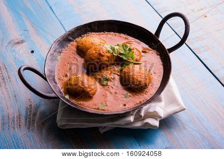 Freshly cooked spicy potato curry in frying pan or Hot and spicy Dum aloo served with tandoori roti or naan or indian bread or chapati and green salad, selective focus
