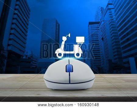 Wireless computer mouse with motor bike icon on wooden table over modern city tower Business internet delivery service concept