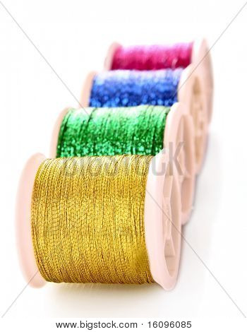 Pile of coloured bobbins of lurex thread isolated on white