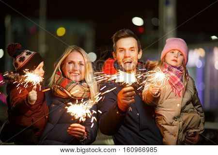 Young family with children with bengal lights on street at night