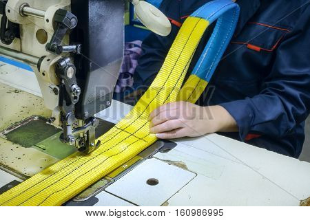 Industrial sewing machine sews a webbing sling. Manufacture of textile slings and tie straps.