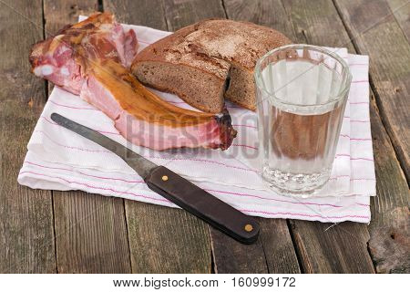 Rye bread ham on edges and a glass of water. On a pure towel bread ham and a knife nearby a glass of water lies. Products on an old wooden table rural style