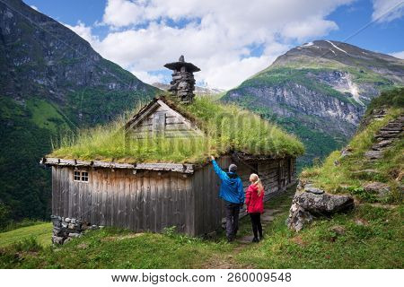 Kagefla - mountain farms on the mountainsides along the Geirangerfjorden fjord. Tourist attraction of Norway. A pair of travelers visiting traditional Scandinavian turf houses