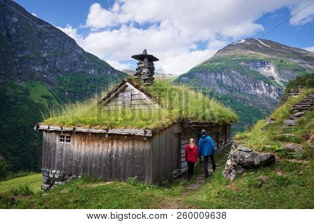 Kagefla - mountain farms with turf houses along the Geirangerfjorden fjord. Tourist attraction of Norway. A pair of travelers visiting traditional Scandinavian architecture