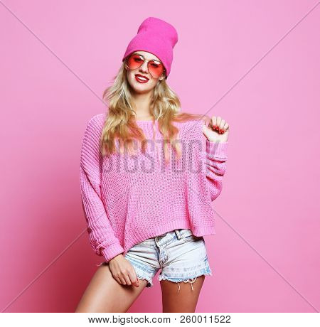 Stylish fashion portrait of trendy casual young woman in pink pulover and hat, posing over pink background