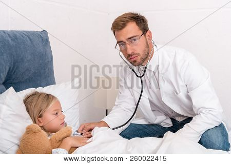 Confident Pediatrician Litening Childs Breath With Stethoscope And Looking At Camera While She Lying