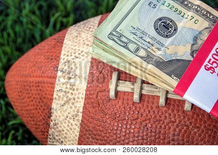 Close Up Of Wrapped Money Stack On Used Football With Green Grass Background