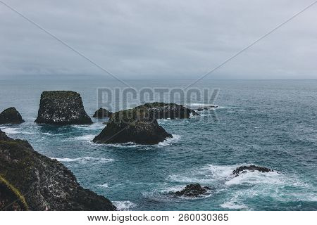 Dramatic Shot Of Rocks In Blue Ocean In Arnarstapi, Iceland On Cloudy Day