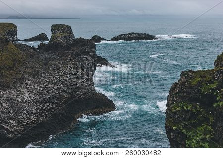 Scenic View Of Mossy Cliffs In Front Of Blue Ocean In Arnarstapi, Iceland On Cloudy Day