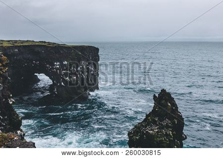Dramatic Shot Of Rocky Cliffs And Stormy Ocean In Arnarstapi, Iceland On Cloudy Day