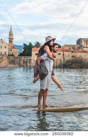 Boyfriend Giving Piggyback To Girlfriend On Ricardova Glava Beach In Budva, Montenegro