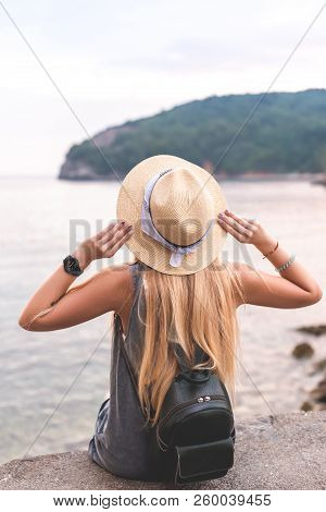 Back View Of Woman Holding Hat And Looking At Adriatic Sea At Ricardova Glava Beach, Budva, Monteneg