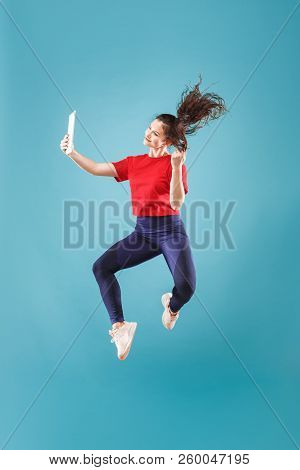 Gadget In Modern Life. Jump Of Young Woman Over Pink Studio Background Using Laptop Or Tablet Gadget