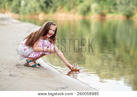 girl playing with a toy sailing ship by the river