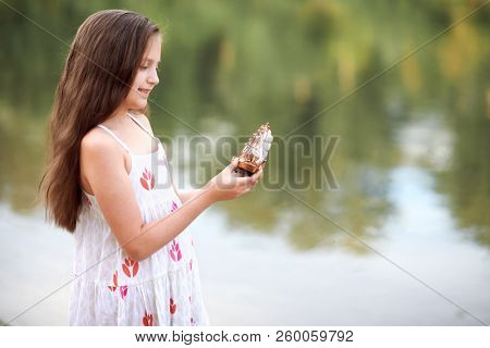 girl playing with a toy sailing ship by the river