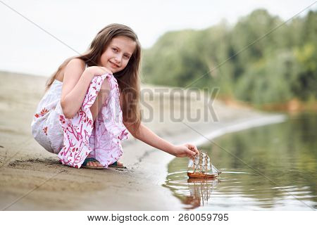 girl playing with a toy sailing ship by the river