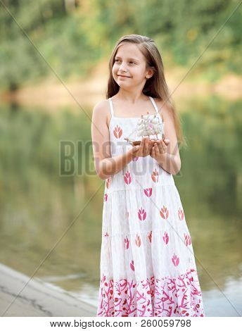 girl playing with a toy sailing ship by the river