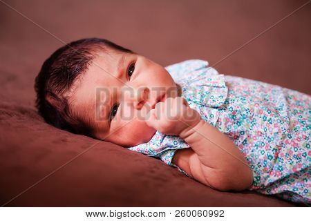 Close up portrait of a cute two weeks old newborn baby girl lying down, eyes open and looking around wearing a floral dress