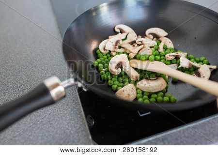 food, culinary and cooking concept - close up of mushrooms with pea in frypan on cooker