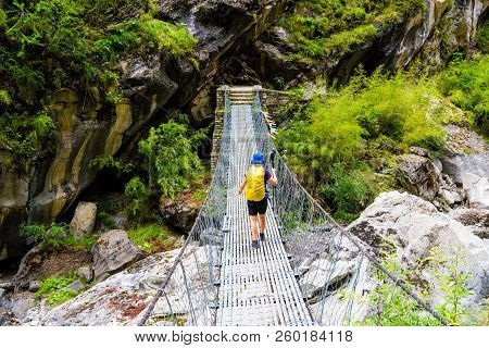 Woman Backpacker On Trekking Path Crossing A Suspended Bridge In Annapurna Conservation Area, Nepal