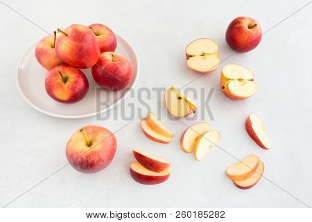 Arrangement Of Whole, Half And Sliced Red Gala Apples On A White Porcelain Plate And White Textured 