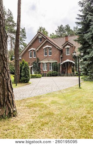 Large Detached House Exterior With Brick Walls And Red Roof Behind A Cobblestone Path And Green Lawn