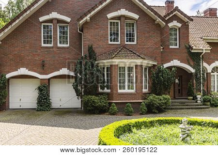 Real Photo Of A Brick House With A Bay Window, Garages And Round Garden In Front Of The Entrance