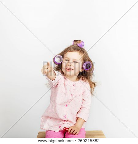Beautiful Little Girl With Curlers On Her Head Looking At Camera And Having Fun At Home. Day Off, Ho