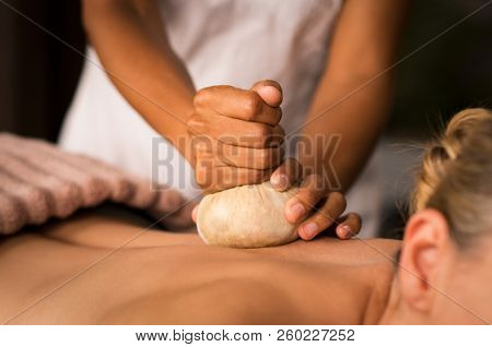 Closeup of masseuse hands holding pinda massage to woman on spa table. Therapist hands giving ayurveda aroma pinda sweda massage to naked lady. Senior woman doing aromatic painkiller massage on back.