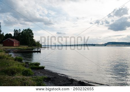 Scenic View Of Mjosa Lake Under Cloudy Sky And Distant Red Cottage, Hamar, Hedmark, Norway