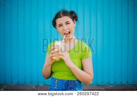 Portrait Of A Girl Against A Bright Blue Wall. Emotional Girl Holding A Plastic Glass With A Refresh