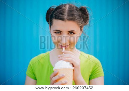 Portrait Of A Girl Against A Bright Blue Wall. Emotional Girl Holding A Plastic Glass With A Refresh
